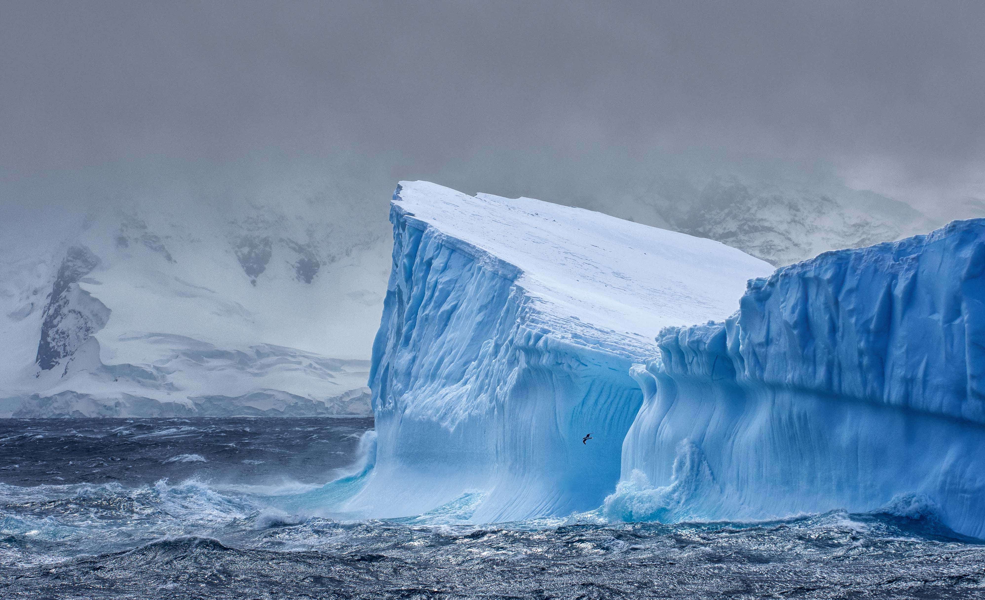 Et stort blåt isbjerg i havet, med et bjerg i baggrunden